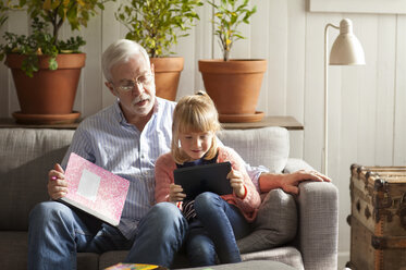 Mädchen, das einen Tablet-Computer benutzt, während es mit seinem Großvater auf dem Sofa zu Hause sitzt - CAVF17615
