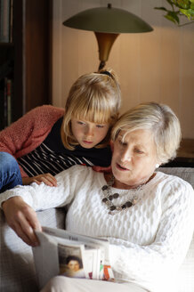 Großmutter zeigt ihrer Enkelin eine Zeitschrift, während sie zu Hause auf dem Sofa sitzt - CAVF17616