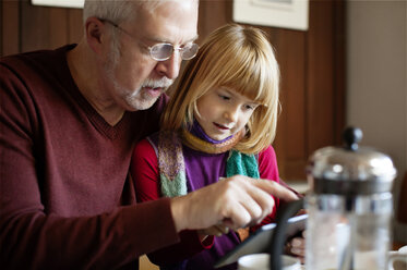 Großvater zeigt seiner Enkelin einen Tablet-Computer, während er am Tisch sitzt - CAVF17630