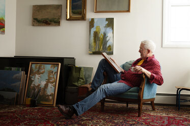 Mann betrachtet ein Gemälde, während er auf einem Sessel sitzt - CAVF17631