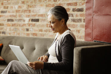 Seitenansicht einer Geschäftsfrau, die einen Laptop benutzt, während sie auf dem Sofa im Büro sitzt - CAVF17637
