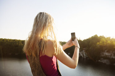 Rückansicht einer jungen Frau, die mit ihrem Smartphone die Natur fotografiert - CAVF17641