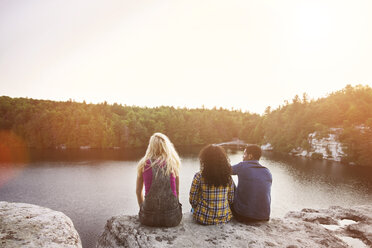 Rückansicht von Freunden, die auf einem Felsen am See sitzen, gegen den klaren Himmel - CAVF17645