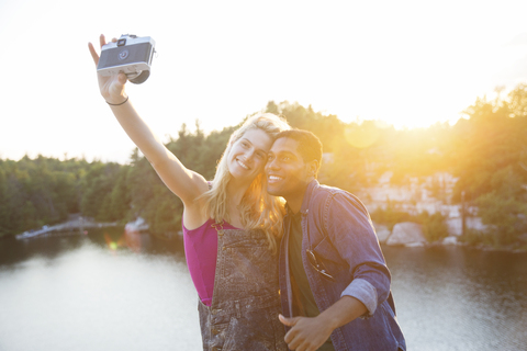 Freunde nehmen Selfie durch Kamera am See bei Sonnenuntergang, lizenzfreies Stockfoto