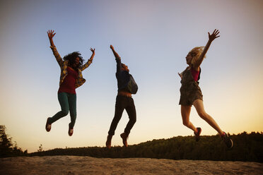 Friends jumping on rock against clear sky during dusk - CAVF17657