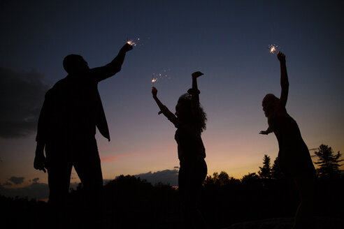 Silhouette von Freunden spielen mit Wunderkerzen gegen den Himmel in der Nacht - CAVF17662