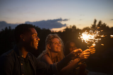 Happy friends holding illuminated sparklers at dusk - CAVF17664