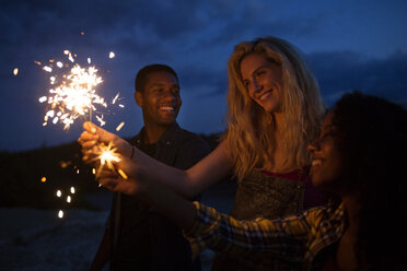 Friends holding illuminated sparklers at night - CAVF17665