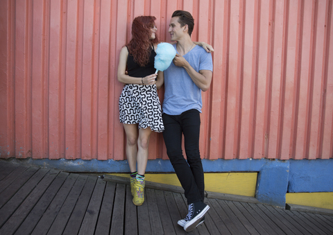 Junges Paar hält Zuckerwatte und steht an der Wand, lizenzfreies Stockfoto