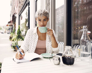 Porträt einer Frau mit Kaffeetasse und Stift in einem Straßencafé - CAVF17687