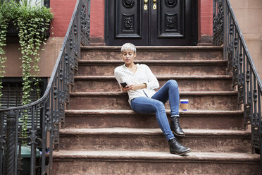 Woman using mobile phone while sitting on steps - CAVF17691