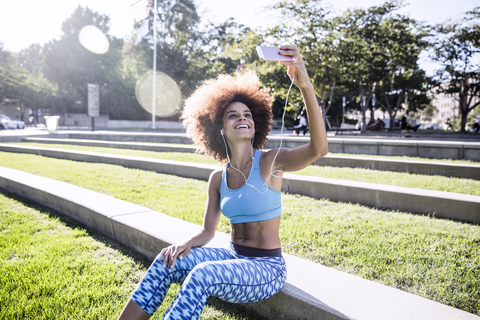 Glückliche Frau, die ein Selfie macht, während sie im Park sitzt, lizenzfreies Stockfoto