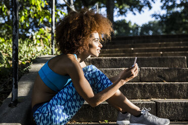 Frau mit Mobiltelefon schaut weg, während sie auf einer Treppe im Park sitzt - CAVF17709