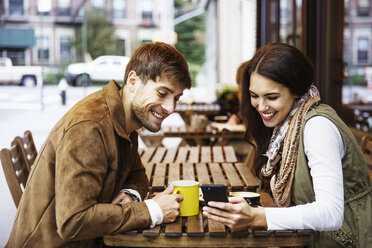 Glückliches Paar schaut auf sein Handy, während es in einem Café Getränke genießt - CAVF17726