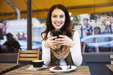 Portrait of woman using mobile phone while sitting at sidewalk cafe - CAVF17727