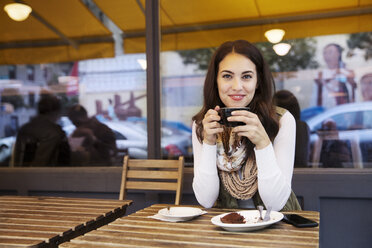 Portrait of woman holding coffee cup while sitting at sidewalk cafe - CAVF17728