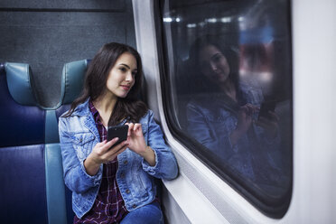 Thoughtful woman with mobile phone looking away while traveling in train - CAVF17738