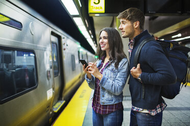 Smiling couple looking away while standing at subway station - CAVF17741