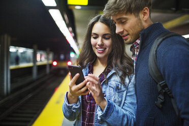 Paar, das ein Mobiltelefon benutzt, während es in einer U-Bahn-Station steht - CAVF17742