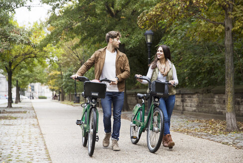 Ehepaar im Gespräch, während es mit dem Fahrrad auf der Straße im Park spazieren geht - CAVF17752