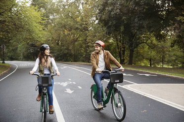 Lächelndes Paar fährt Fahrrad auf der Straße im Park - CAVF17753