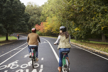Rückansicht eines glücklichen Paares beim Fahrradfahren auf einer Straße im Park - CAVF17754