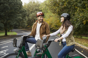 Smiling couple talking while standing with bicycles on road at park - CAVF17755