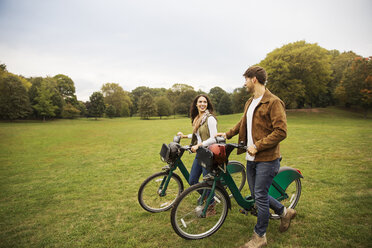 Glückliches Paar unterhält sich beim Spaziergang mit Fahrrädern auf einer Wiese - CAVF17757
