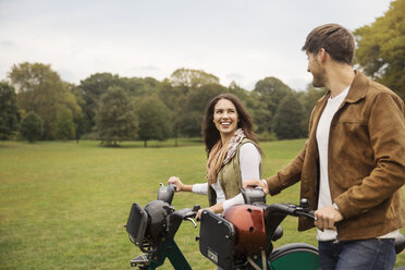 Glückliches Paar im Gespräch beim Spaziergang mit Fahrrädern im Park - CAVF17758