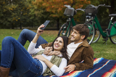 Couple taking selfie while relaxing on blanket at park - CAVF17761