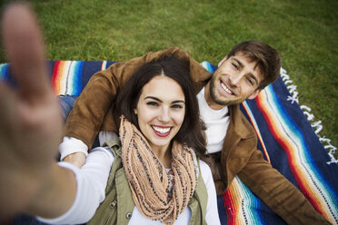 Porträt eines glücklichen Paares auf einer Decke im Park liegend - CAVF17762