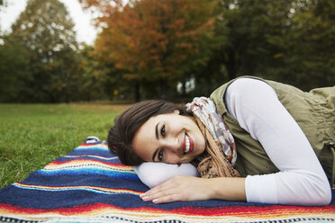 Portrait of happy woman lying on blanket at park - CAVF17765