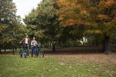 Paar im Gespräch beim Spaziergang mit Fahrrädern im Park - CAVF17767