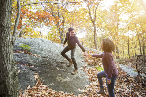 Mann hilft seiner Freundin beim Gehen auf einem Felsen im Wald, lizenzfreies Stockfoto