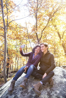 Paar, das ein Selfie macht, während es auf einem Felsen im Wald sitzt - CAVF17773