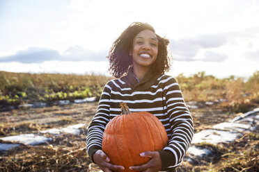 Portrait of woman carrying pumpkin while standing in farm against sky - CAVF17780