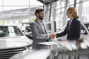 Car saleswoman and male customer handshaking in car dealership showroom - CAIF19974