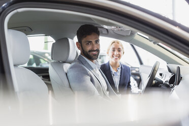 Porträt einer lächelnden, selbstbewussten Autoverkäuferin und eines männlichen Kunden auf dem Fahrersitz eines neuen Autos in einem Autohaus - CAIF19982