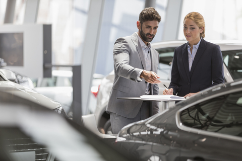 Autoverkäufer, die sich treffen und ein neues Auto im Ausstellungsraum eines Autohauses begutachten, lizenzfreies Stockfoto