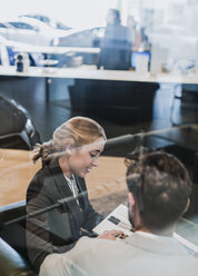 Car saleswoman explaining brochure to male customer in car dealership - CAIF19991