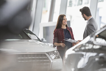 Car saleswoman showing brochure to male customer in car dealership showroom - CAIF19999