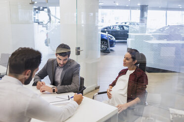 Car salesman explaining financial contract paperwork to pregnant couple customers in car dealership office - CAIF20006