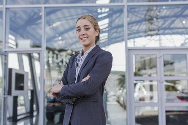 Porträt einer selbstbewussten, lächelnden Autoverkäuferin, die vor einem Ausstellungsraum eines Autohauses steht - CAIF20013