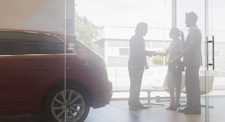 Autoverkäufer beim Händeschütteln mit einem Kundenpaar im Ausstellungsraum eines Autohauses - CAIF20017