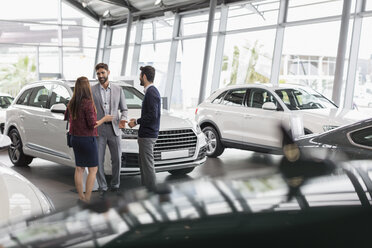 Autoverkäufer im Gespräch mit einem Kundenpaar im Ausstellungsraum eines Autohauses - CAIF20021