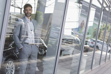 Portrait confident car salesman standing in window at car dealership showroom - CAIF20022