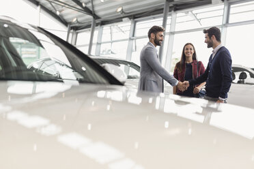 Car salesman shaking hands with couple customers in car dealership showroom - CAIF20027