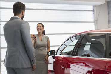 Car salesman giving keys to new car to female customer in car dealership - CAIF20031