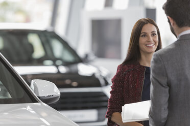 Smiling female customer listening to car salesman in car dealership showroom - CAIF20039