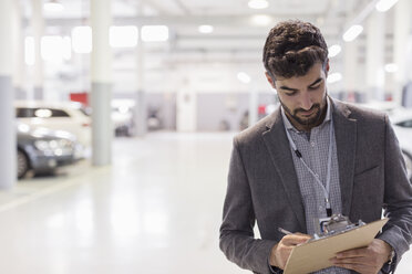 Autoverkäufer schreibt auf Klemmbrett in Autohaus Autoreparaturwerkstatt - CAIF20042